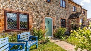 A stone house with a green door, two windows with metal bars, and a small garden with a bench. - Host Stay Honeysuckle Cottage (Cromer)