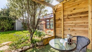 A wooden cabin with a glass table and chairs, surrounded by a garden and a view of a house. - Host Stay Honeysuckle Cottage (Cromer)