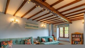 A cozy living room with exposed wooden beams, a teal sofa, a bookshelf, and a window with a lattice design. - Host Stay Honeysuckle Cottage (Cromer)