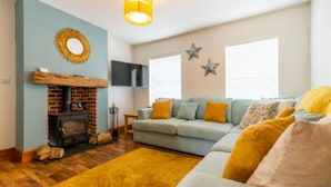 A cozy living room with a fireplace, a sofa with orange cushions, and a yellow rug. - Host Stay Pilgrims Rest (Cromer)