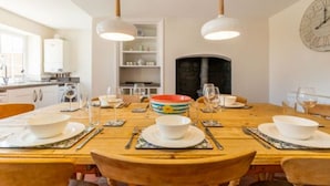 A dining area with a wooden table set for four, surrounded by chairs. There are hanging pendant lights above the table. - Host Stay Pilgrims Rest (Cromer)