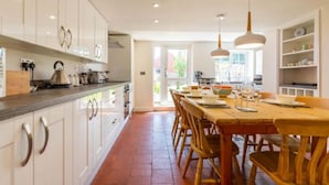 A modern kitchen with white cabinets, a wooden dining table, and pendant lighting. - Host Stay Pilgrims Rest (Cromer)