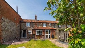 A two-story brick house with a tiled roof, a front door, and a small front yard with a lawn and a few plants. - Host Stay Pilgrims Rest (Cromer)