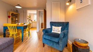 A living room with a blue armchair, a dining table with yellow chairs, and a kitchen in the background. - Host Stay The Courtyard (King's Lynn)