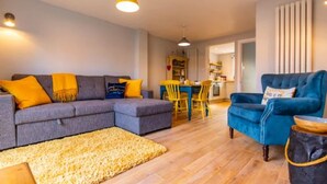 A modern living room with a sectional sofa, a blue armchair, and a yellow rug. - Host Stay The Courtyard (King's Lynn)