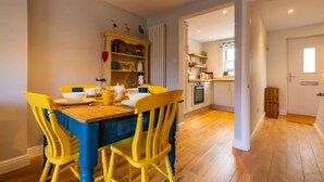 A dining area with a wooden table and yellow chairs, a kitchen in the background, and a hallway leading to another room. - Host Stay The Courtyard (King's Lynn)