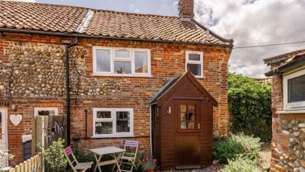 A stone house with a tiled roof, a small wooden shed, and a garden with a table and chairs. - Host Stay Sandpipers (Holt)