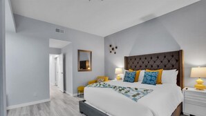 A bedroom with a large bed, a nightstand, a mirror, and a door leading to another room. - Hollywood Glam Hideaway (Palm Springs)