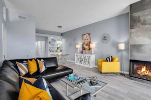 A modern living room with a black leather sofa, a yellow armchair, a glass coffee table, and a fireplace. - Hollywood Glam Hideaway (Palm Springs)
