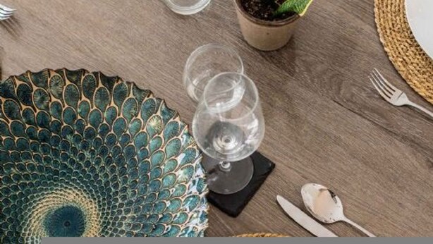 A wooden table with a decorative plate, two wine glasses, a potted plant, and cutlery. - Host Stay Willow Barn (Norwich)