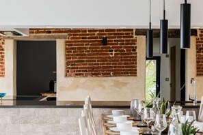 A dining area with a brick wall, modern pendant lights, and a table set for a meal. - Host Stay Willow Barn (Norwich)
