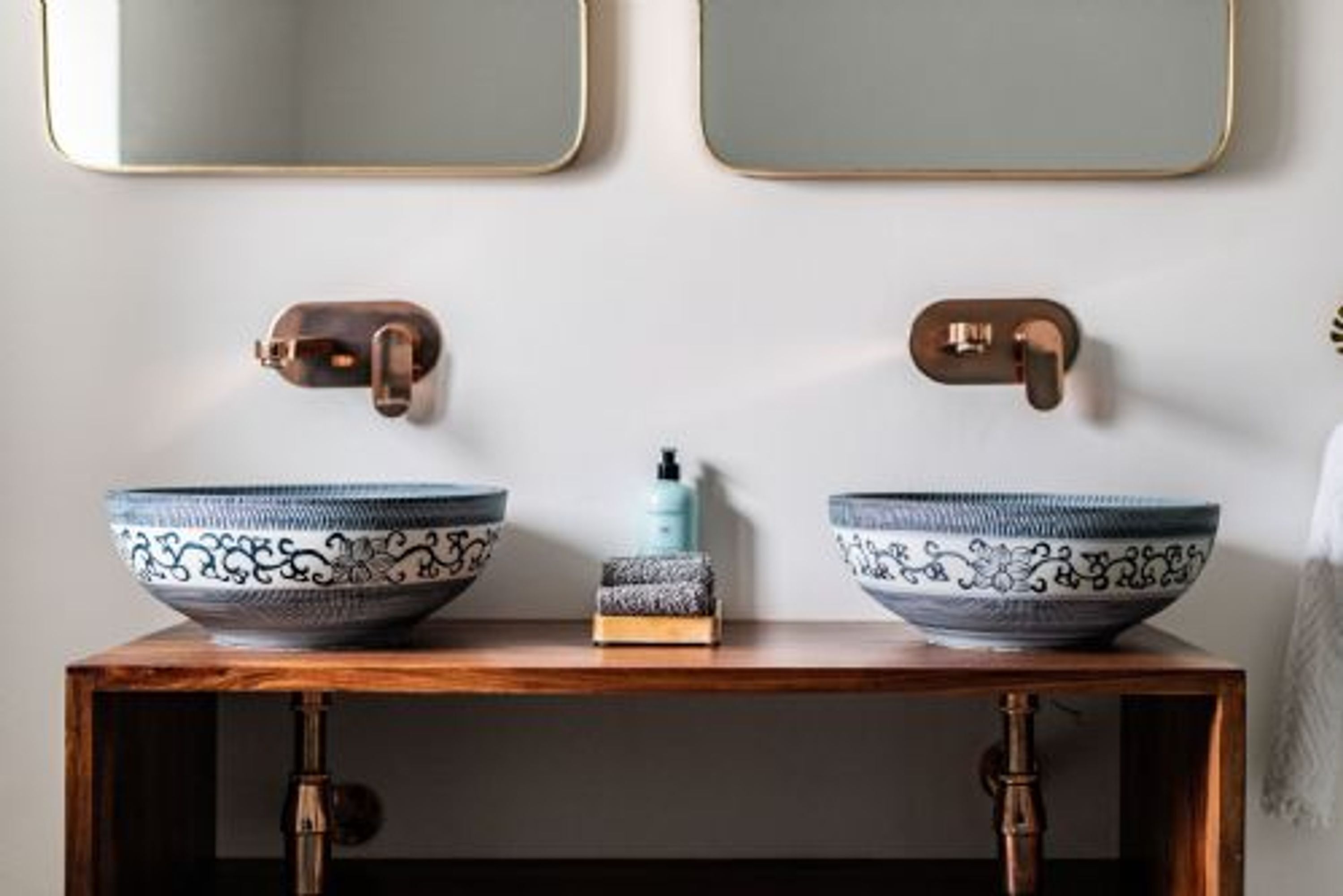 A bathroom with two large, ornate bowls on a wooden vanity, a soap dispenser, and a towel rack.