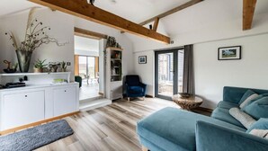 A modern living room with a blue sofa, a white cabinet, and a wooden ceiling beam. - Host Stay Willow Barn (Norwich)