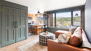 Eine moderne Küche mit Barbereich, großen Fenstern mit Aussicht und einer gemütlichen Sitzecke mit Sofa und Hocker.