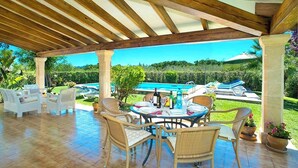 Eine überdachte Terrasse mit Rattanmöbeln, einem Pool und Blick auf die Landschaft.