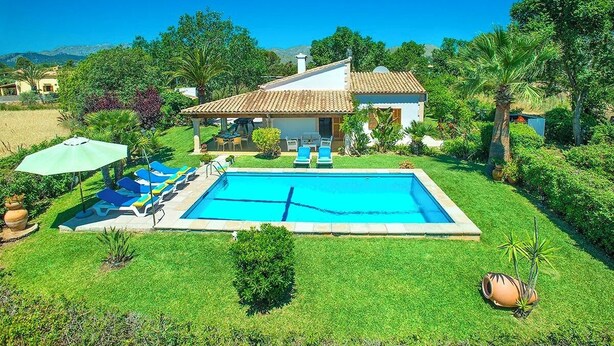 Ein Haus mit Schwimmbad, umgeben von viel Grün und blauem Himmel.