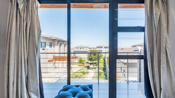A room with a large sliding glass door leading to a balcony with a view of neighboring buildings and a tree.
