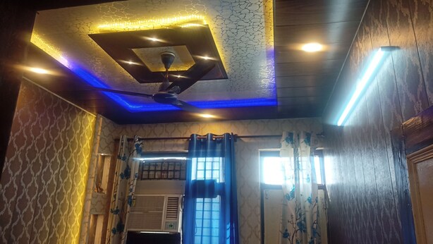A room with a ceiling fan, patterned walls, and a window with curtains. - ASHIANA HOME STAY  (Jammu)