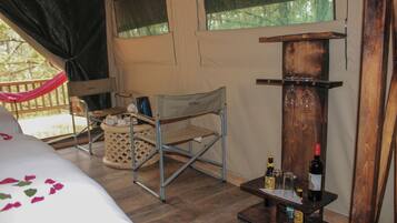 A cozy room with a bed, a small table with wine bottles and glasses, a chair, and a hammock.