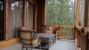 A wooden deck with a table and chairs, a window with curtains, and a view of a forest. - Kuriftu Entoto Adventure Park (Addis Ababa)