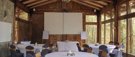 Un salón de conferencias con mesas y sillas redondas, pizarrones y una pantalla para proyector.