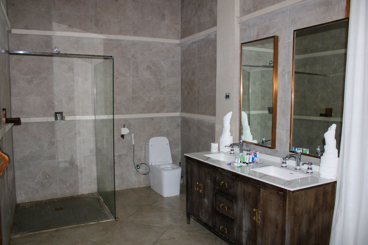 Une salle de bain moderne dotée d’une douche à parois de verre, de toilettes et d’un meuble-lavabo avec deux vasques et un grand miroir.
