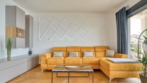 Ein modernes Wohnzimmer mit Ecksofa, Glastisch und einer Zierverkleidung an der Wand.