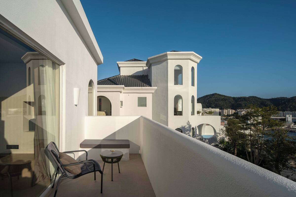 En balkon med stol og bord, med udsigt til en bygning med hvælvede vinduer og en hvid facade.
