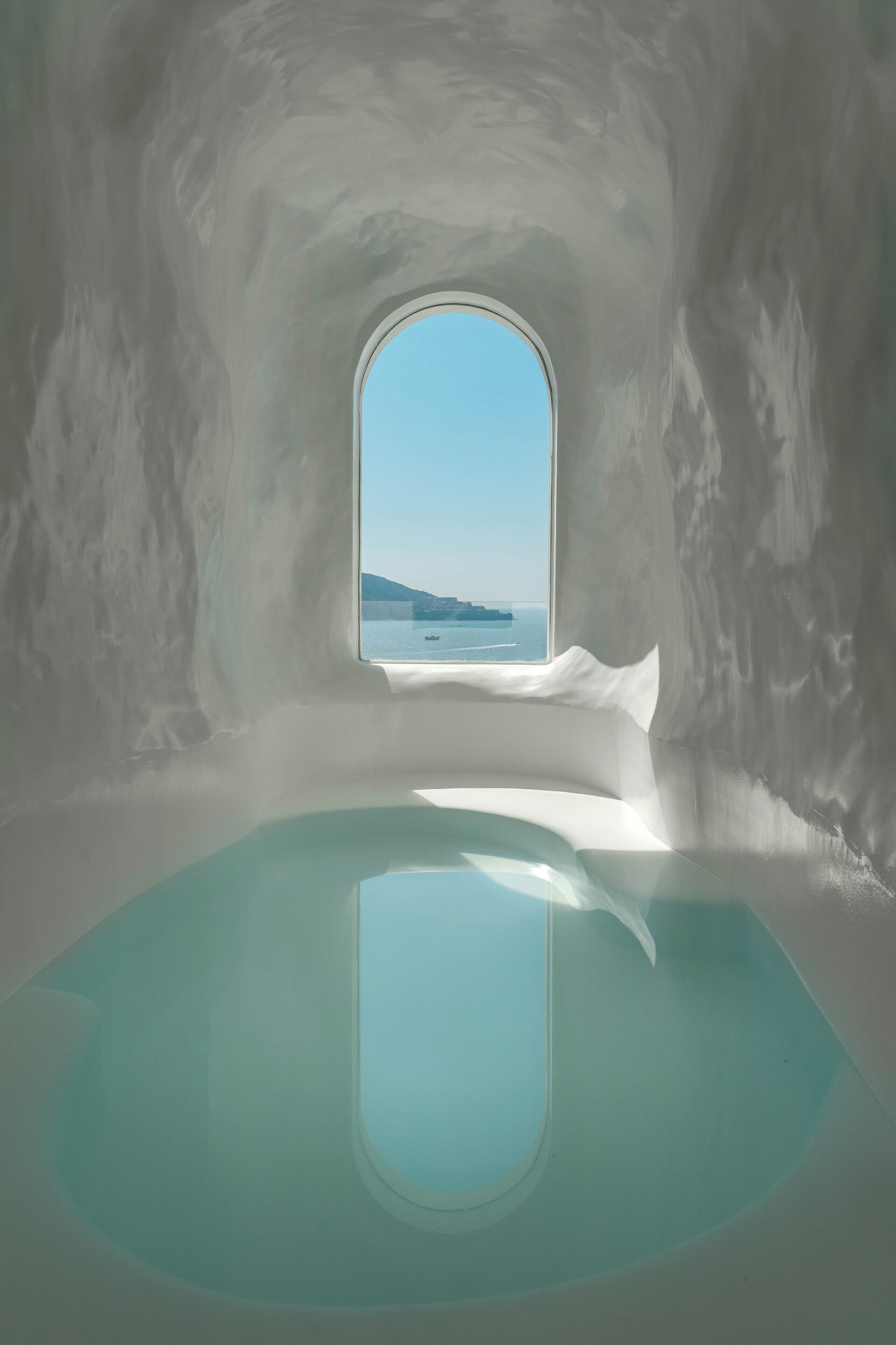 A room with a large window offering a view of the sea and a distant island.
