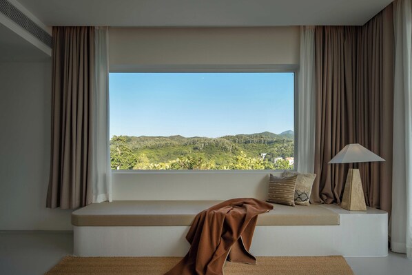 Una habitación con un ventanal grande, una banca, una lámpara y vistas a colinas verdes.