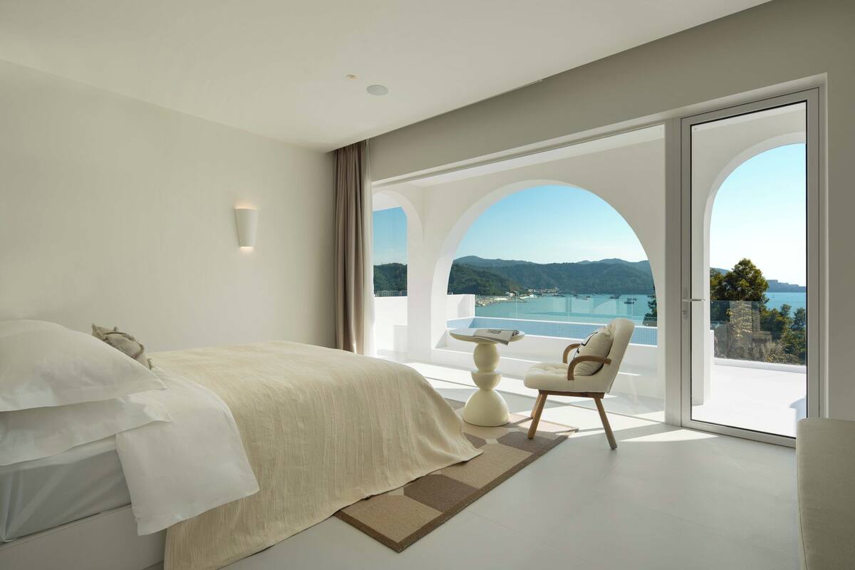 Et soveværelse med en stor seng, havudsigt og en balkon med bord og stol.