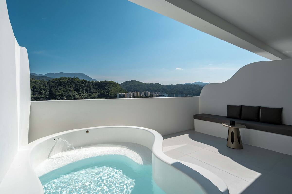 Et moderne udendørs badeværelse med jacuzzi, opholdsområde med bord samt udsigt til bjerge og bygninger.