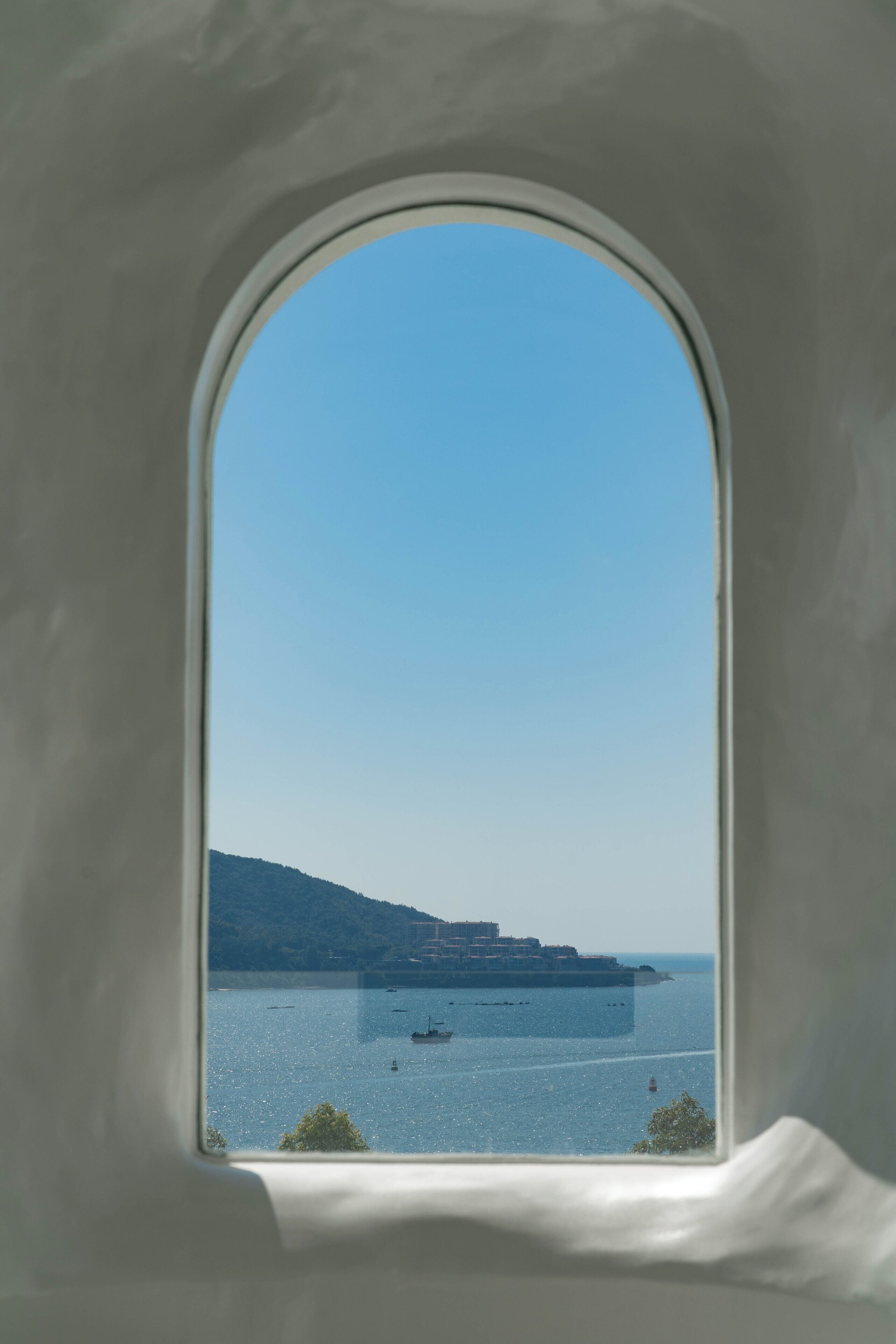 Une vue à travers une fenêtre, avec un ciel dégagé, une eau calme et des reliefs lointains.