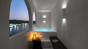 Une salle de bain moderne avec une baignoire, un banc et une vue sur un lac au crépuscule.