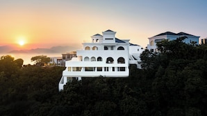 Un bâtiment moderne de couleur blanche, doté de nombreux balcons et offrant une vue sur le coucher de soleil en mer.
