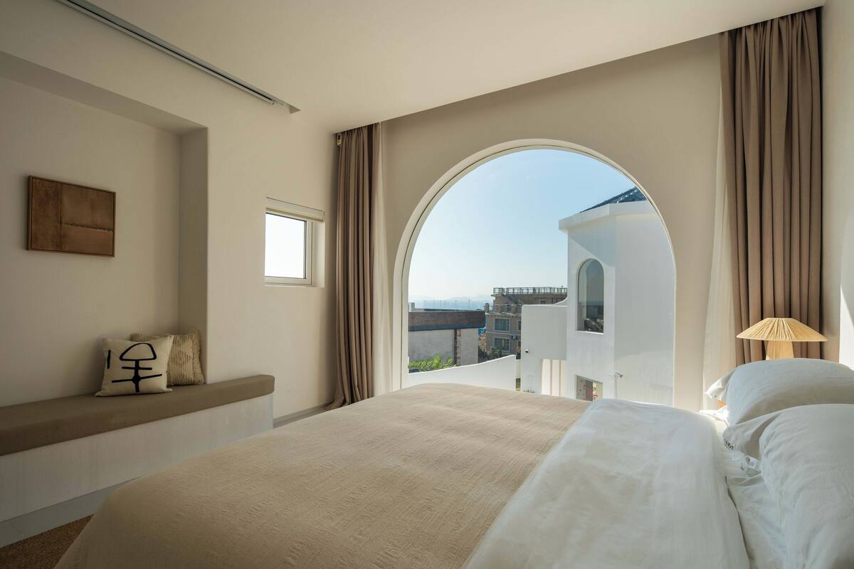Et hotelværelse med en stor seng, udsigt gennem et buet vindue og en balkon med udsigt til en bro.