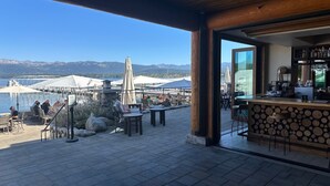 An outdoor terrace with tables and chairs, a bar area, and a view of the lake and mountains. - Everwoods Aframe - Modern Luxury, Cozy Mountain Retreat (McCall)