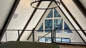 A high-ceilinged room with a bed, a large window, and a wooden ceiling structure. - Everwoods Aframe - Modern Luxury, Cozy Mountain Retreat (McCall)