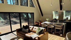 A modern living room with a leather sofa, wooden coffee table, and a dining area with a kitchen in the background. - Everwoods Aframe - Modern Luxury, Cozy Mountain Retreat (McCall)