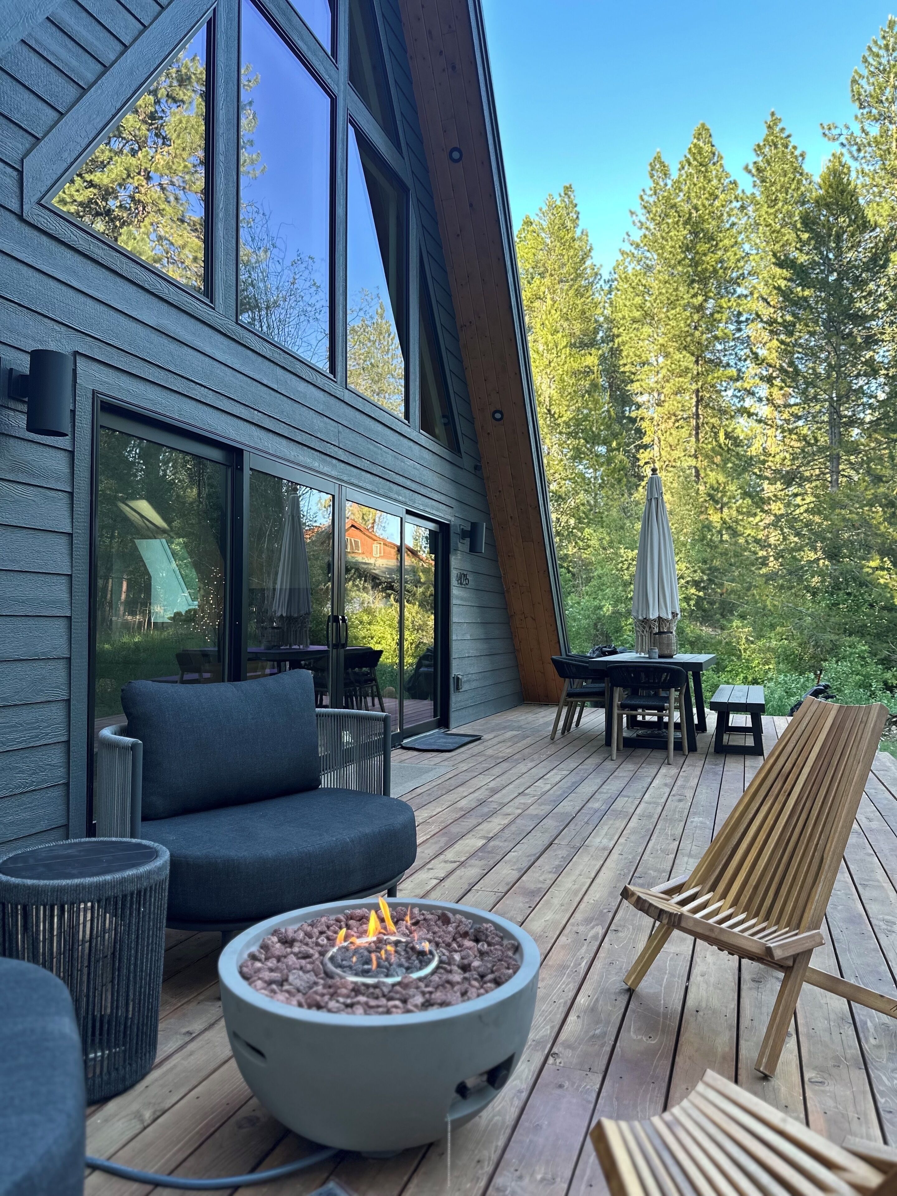 Eine moderne Terrasse mit Feuerstelle, Gartenmöbeln und Blick auf einen bewaldeten Bereich.