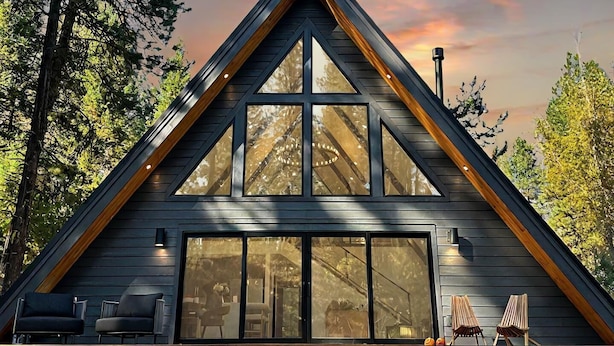 A modern, triangular wooden cabin with large windows, a wooden deck, and outdoor seating. - Everwoods Aframe - Modern Luxury, Cozy Mountain Retreat (McCall)