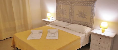 Une chambre d’hôtel avec une couvre-lit jaune, deux lampes de chevet, une table de chevet avec une lampe, une tête de lit décorative et un tapis à motifs.
