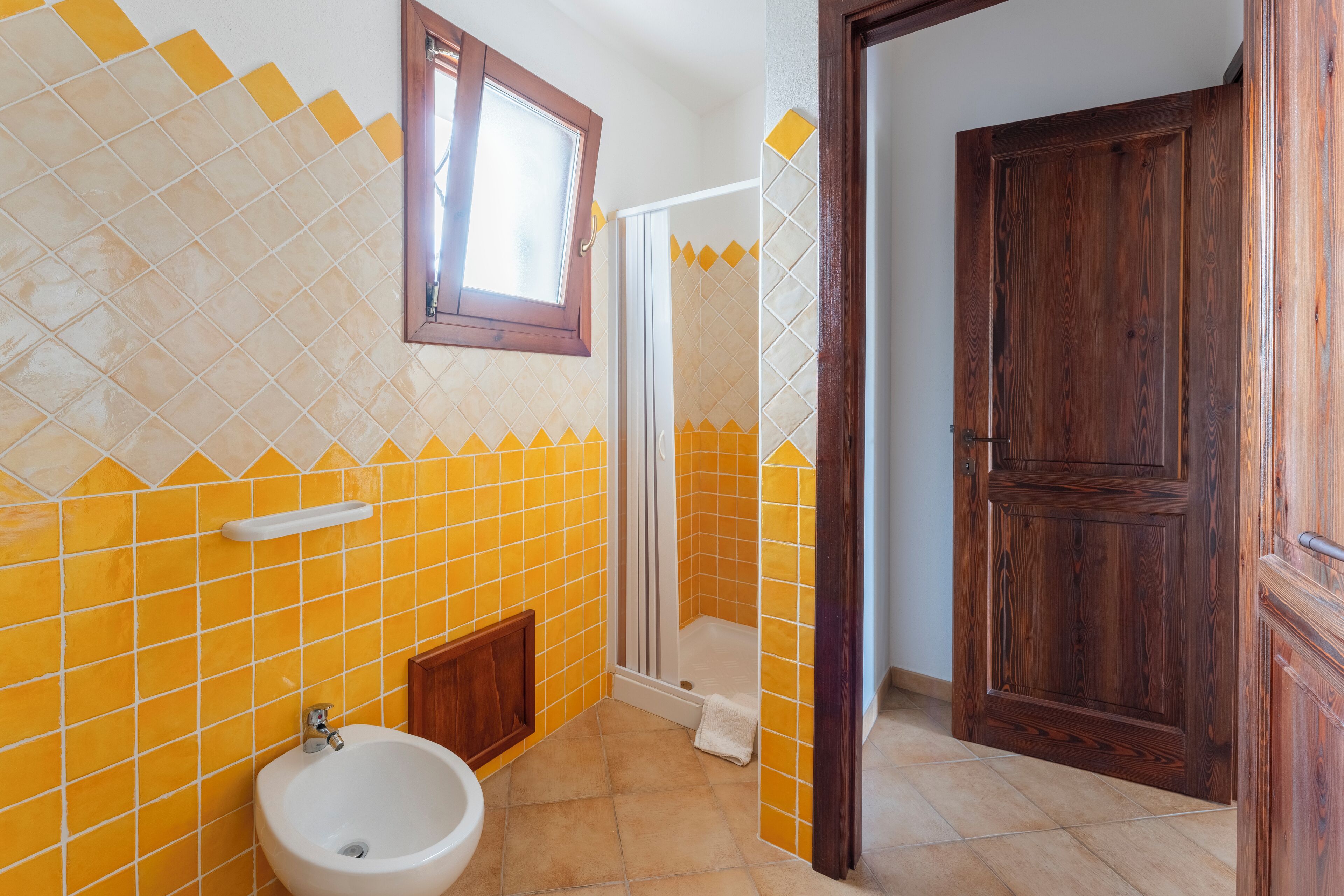 A bathroom with yellow and white tiles, a white sink, a wooden door, and a shower area.