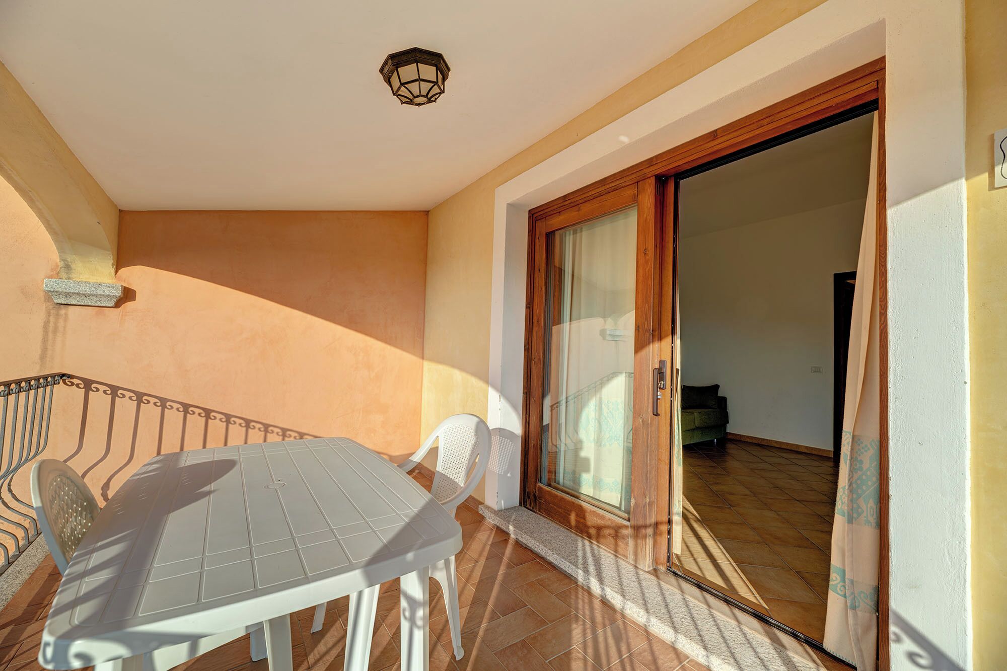 A balcony with a table and chairs, a wooden door, and a tiled floor.