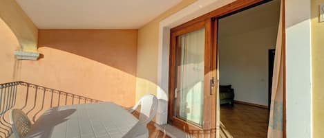 Un balcón con mesa y sillas, una puerta de madera y piso de baldosas.