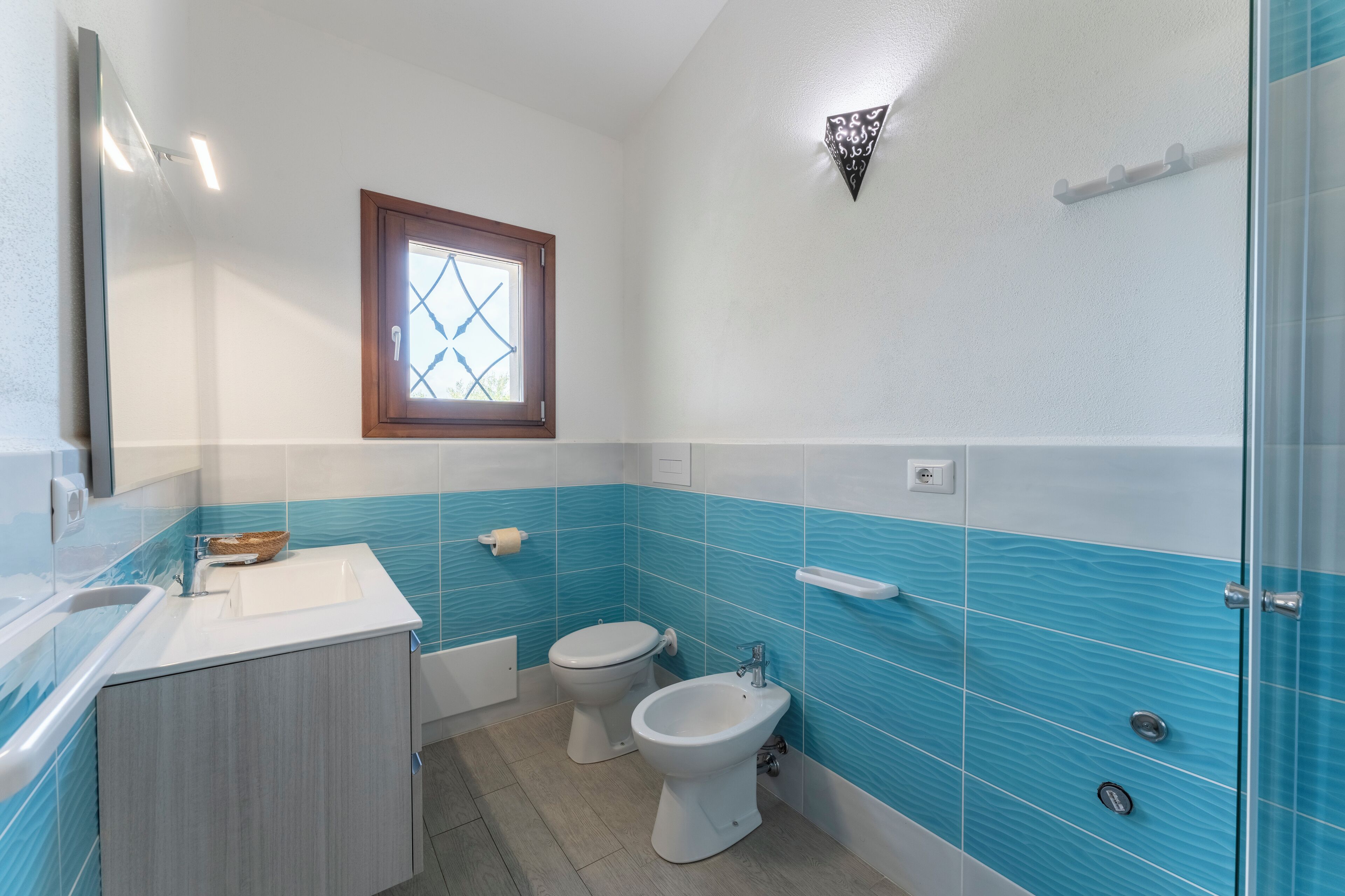 A bathroom with two toilets, a bidet, a sink, and a mirror.