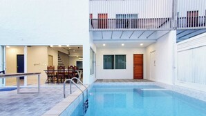 A modern indoor pool area with a clear view of the pool, a wooden bench, and a dining area with chairs. - The villa seamlessly blends modern design, refined aesthetics and serene comfort (Muang Pattaya)