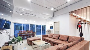 A modern living room with a large brown sofa, a glass coffee table, and a dining area with wooden furniture. - The villa seamlessly blends modern design, refined aesthetics and serene comfort (Muang Pattaya)