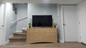 Habitació amb televisió de pantalla plana sobre una petita taula de fusta, una escala i una porta.