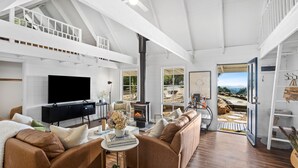 Ein geräumiges Wohnzimmer mit großem Fernseher, Ledersofas, einem Kamin und Blick ins Freie.